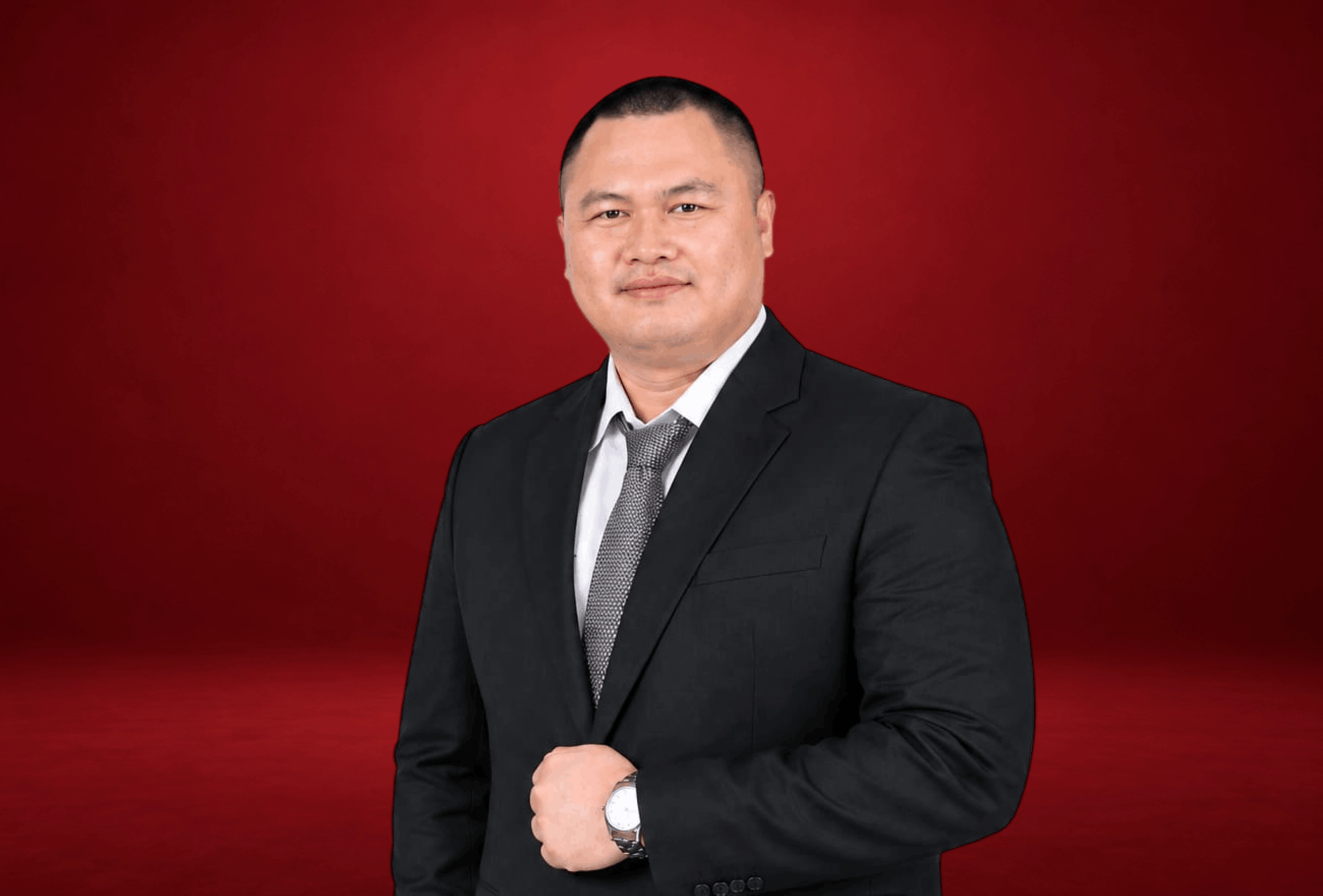 Ridho I. Ginting in a studio portrait, wearing a dark suit with a tie, standing with a composed and professional expression in a clean corporate studio background